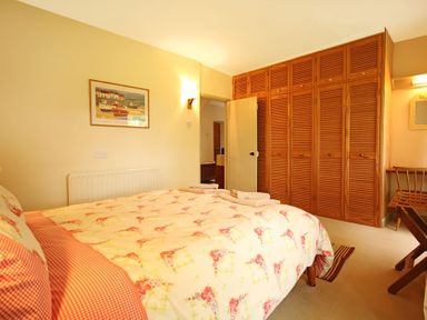 A bedroom with a bed covered in floral bedding a wooden wardrobe and a chair at Perth Hwfa in Malltraeth
