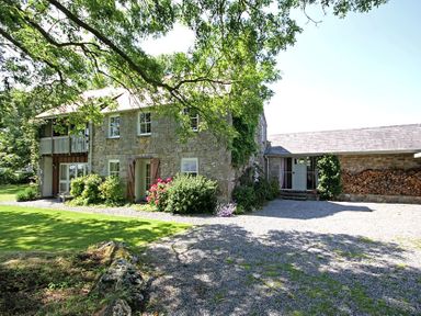 An exterior view of a stone house with a garden and a gravel driveway at Perth Hwfa in Malltraeth