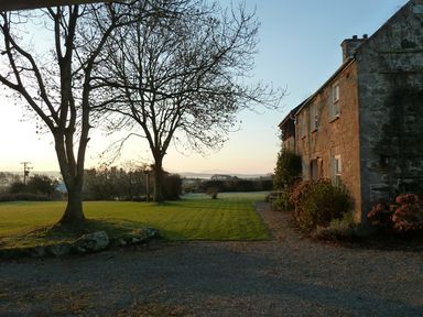 A stone house with bushes and trees on a lawn at Perth Hwfa in Malltraeth