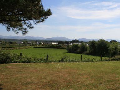 A field with grass and trees with mountains and houses in the background at Perth Hwfa in Malltraeth