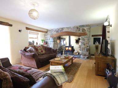 A living room with sofas a wooden coffee table a stone fireplace and a television at Pen Y Bont in Pontllyfni