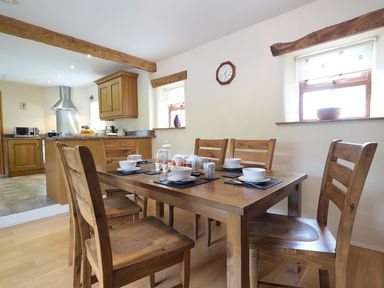 A wooden dining table set with bowls cups and eggs in a kitchen with wooden cabinets and beams at Pen Y Bont in Pontllyfni