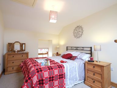A bedroom with a double bed with pillows and a patterned blanket with wooden dressers and lamps at Pen Y Bont in Pontllyfni