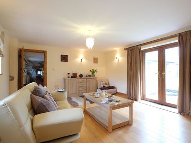 A living room with a beige sofa coffee table sideboard and glass doors with curtains at Pen Y Bont in Pontllyfni