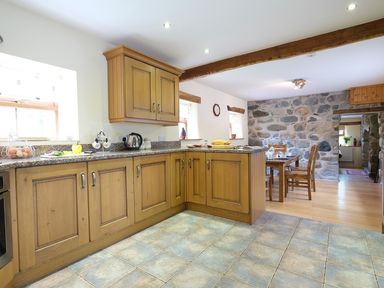 A kitchen with wooden cabinets and granite countertops connected to a dining area with a wooden table and chairs at Pen Y Bont in Pontllyfni