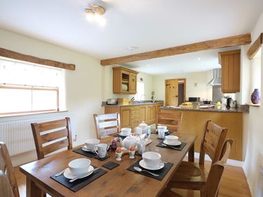 A dining table set for breakfast with bowls mugs and eggs in a kitchen with wooden cabinets and beams at Pen Y Bont in Pontllyfni