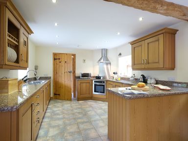 A kitchen with wooden cabinets granite countertops a tiled floor a wooden door and cooking appliances at Pen Y Bont in Pontllyfni