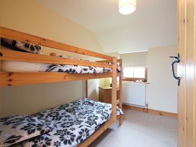 A bedroom with wooden bunk beds and a wooden dresser by the window at Pen Y Bont in Pontllyfni