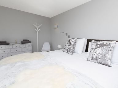 A bedroom with a double bed white and patterned pillows a white dresser with folded towels a white chair and a coat rack at Rhyd Angharad Barns in Rhydwyn