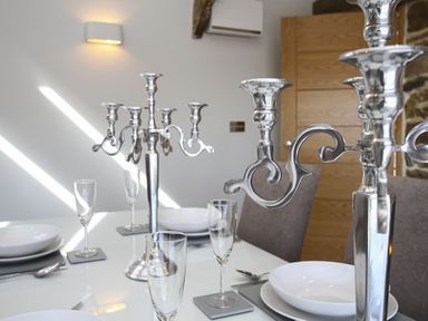 A dining table set with plates, glasses, and silver candelabras in a dining room at Rhyd Angharad Barns in Rhydwyn