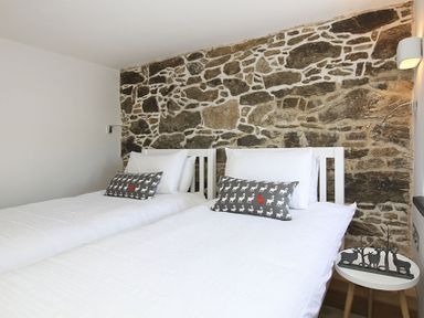 A bedroom with two single beds with white bedding and gray decorative pillows in front of a stone wall at Rhyd Angharad Barns in Rhydwyn