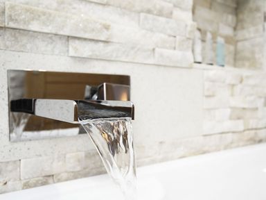 Water flowing from a modern wall-mounted faucet with a stone tile backsplash at Rhyd Angharad Barns in Rhydwyn