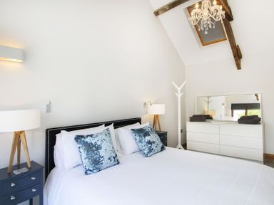A bedroom with a bed with pillows two bedside tables with lamps a dresser with a mirror and a chandelier at Rhyd Angharad Barns in Rhydwyn