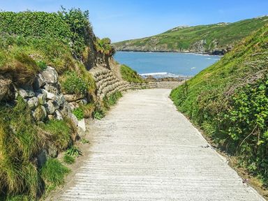 A concrete pathway leading to the sea between grassy hills and stone walls at Rhyd Angharad Barns in Rhydwyn
