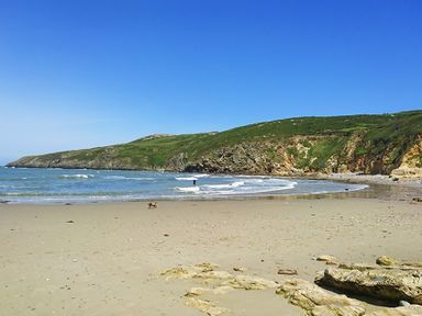 A sandy beach with rocks and a person in the water near cliffs and green hills at Rhyd Angharad Barns in Rhydwyn