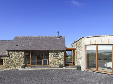A stone house with large wooden framed windows and a gravel driveway at Rhyd Angharad Barns in Rhydwyn