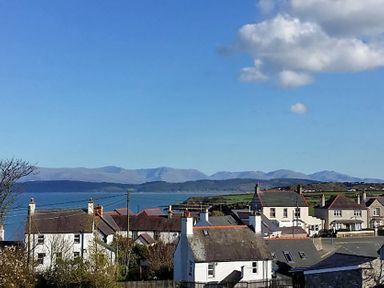 A coastal village with houses in the foreground and mountains in the background at Seiriol View in Moelfre