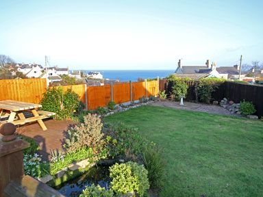 A garden with a wooden picnic table a small pond green grass and an ocean view at Seiriol View in Moelfre