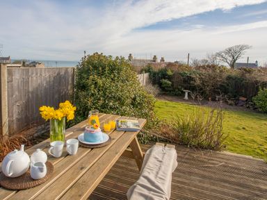 A wooden picnic table with a teapot cups flowers cake and orange juice in a garden at Seiriol View in Moelfre