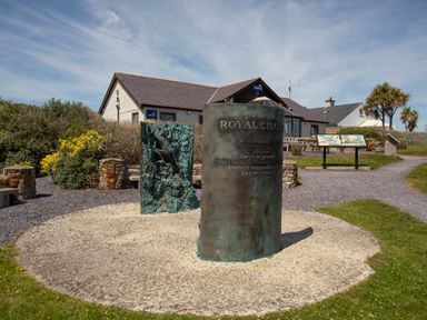 An outdoor memorial with sculptures and plaques near a building with lifeboats signs at Seiriol View in Moelfre