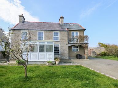 A stone house with a front porch and a small tree on a lawn at Seiriol View in Moelfre