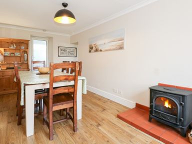 A dining room with a table and wooden chairs a wood burning stove and a wooden cabinet at Seiriol View in Moelfre