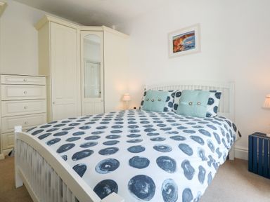 A bedroom with a bed with polka dot bedding and two blue cushions next to wardrobes and a chest of drawers at Seiriol View in Moelfre
