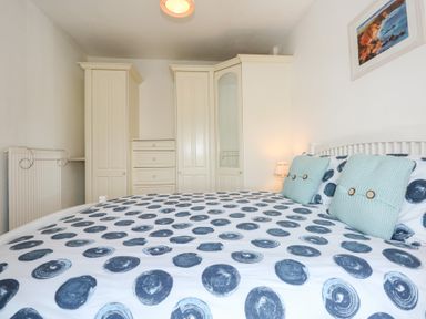 A bedroom with a bed with patterned bedding two cushions built in wardrobes a bedside lamp and a wall painting at Seiriol View in Moelfre