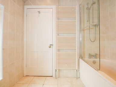 A bathroom with a white door radiator and a bathtub with shower at Seiriol View in Moelfre