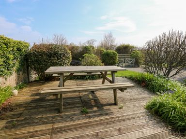 A wooden picnic table on a wooden deck surrounded by bushes and plants at Seiriol View in Moelfre