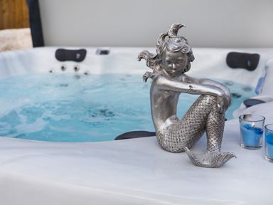 A silver mermaid statue on the edge of a hot tub with blue water and two blue candles at The Mermaid in Brynsiencyn