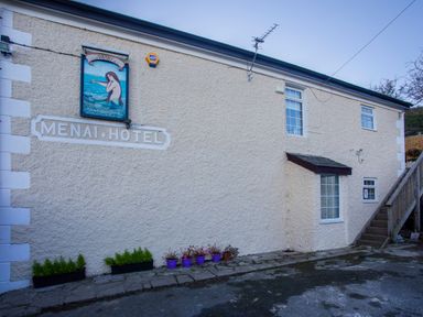 Exterior view of a building with sign Menai Hotel and Mermaid Inn with windows stairs and flower pots at The Mermaid in Brynsiencyn