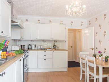 A kitchen with white cabinets wooden countertops and a dining table with chairs at The Mermaid in Brynsiencyn