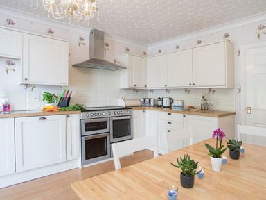 A kitchen with white cabinets a wooden table with plants and candles at The Mermaid in Brynsiencyn