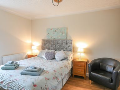 A bedroom with a bed with floral bedding two bedside tables with lamps and a black armchair at The Mermaid in Brynsiencyn