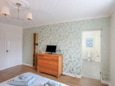 A bedroom with a wooden dresser a tall shelf and an open door to a bathroom at The Mermaid in Brynsiencyn