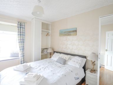 A bedroom with a double bed two bedside tables with lamps an open wardrobe window with curtains and a wall painting at The Mermaid in Brynsiencyn