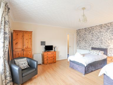 A bedroom with two beds a black armchair wooden wardrobe chest of drawers and patterned wallpaper at The Mermaid in Brynsiencyn