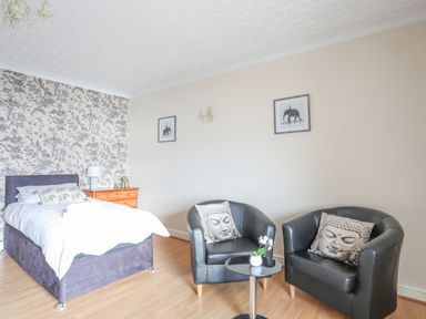 A bedroom with a bed bedside table two black armchairs and a small round table at The Mermaid in Brynsiencyn