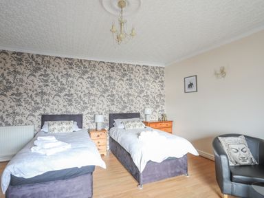 A bedroom with two single beds bedside tables and a black chair at The Mermaid in Brynsiencyn