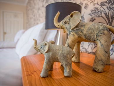 Two wooden elephant figurines on a wooden surface with a black lamp and a white bed in the background at The Mermaid in Brynsiencyn
