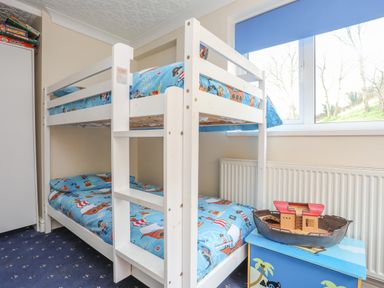 A children's bedroom with a white bunk bed and pirate-themed bedding a toy boat on a blue chest under a window at The Mermaid in Brynsiencyn