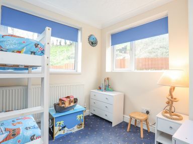 A children's bedroom with bunk beds a toy chest a white dresser and a lamp at The Mermaid in Brynsiencyn