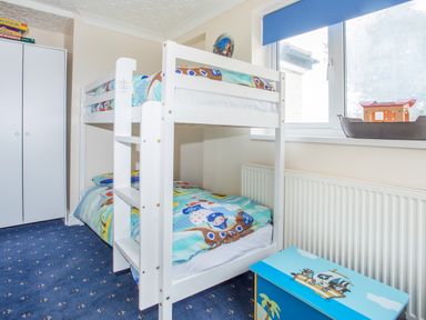 A child's bedroom with a white bunk bed a blue carpet a blue toy chest and a window at The Mermaid in Brynsiencyn