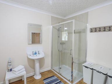 A bathroom with a sink mirror shower and three laundry baskets at The Mermaid in Brynsiencyn