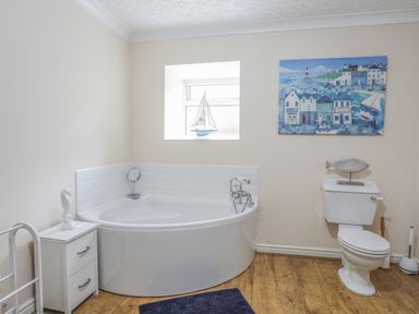 A bathroom with a corner bathtub and a toilet with a fish decoration and a small drawer unit at The Mermaid in Brynsiencyn