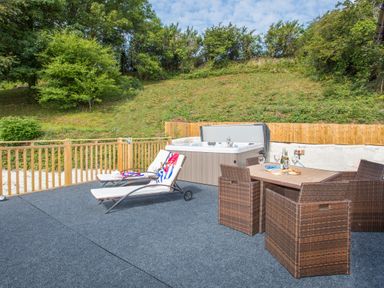 An outdoor patio with two lounge chairs a hot tub and a dining table with chairs and drinks at The Mermaid in Brynsiencyn