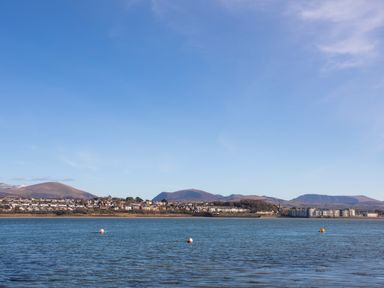 A body of water with buoys and a residential area with hills in the background at The Mermaid in Brynsiencyn