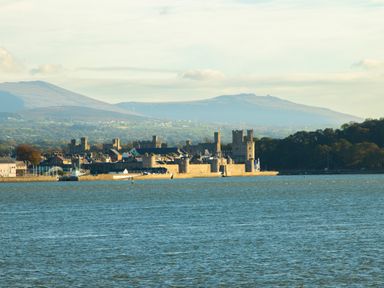 A castle by the water with mountains in the background at The Mermaid in Brynsiencyn