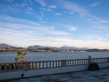 A waterfront view with a stone balustrade and distant buildings across the water at The Mermaid in Brynsiencyn